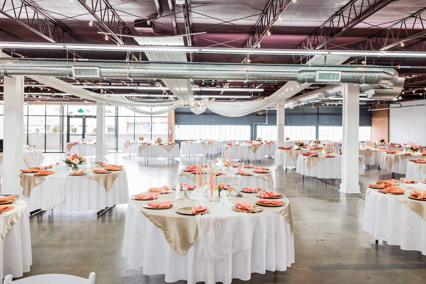 A wide view of a reception room with tables, ceiling drapery and a window wall.